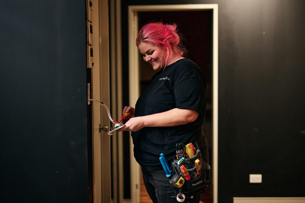 Empowered Electrical owner, and part-time comedian, Caitlin Maggs repairing some light fixtures in her office in Belconnen. 11 May 2023